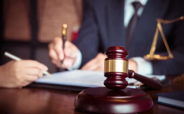 Pessoas escrevendo em documento formal com martelo da justiça ao lado